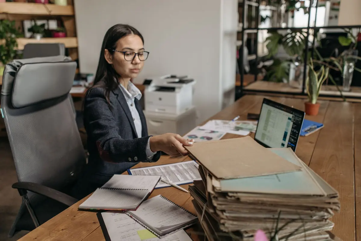 A sales professional at a desk working through a stack of documents beside a laptop.